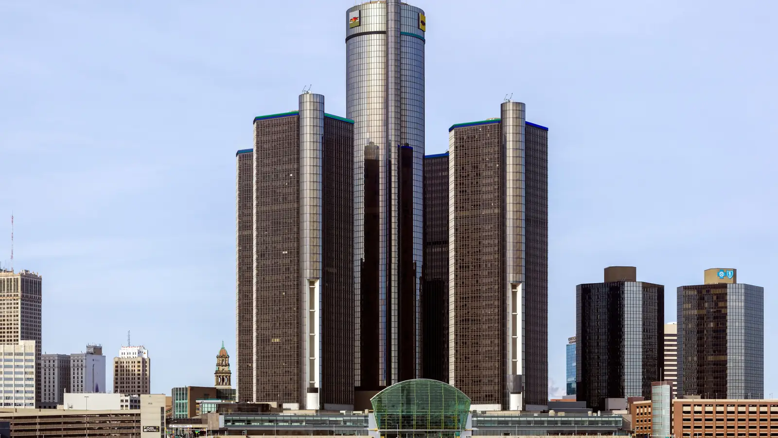 The Renaissance Center towers on the Detroit riverfront under a pale blue sky.