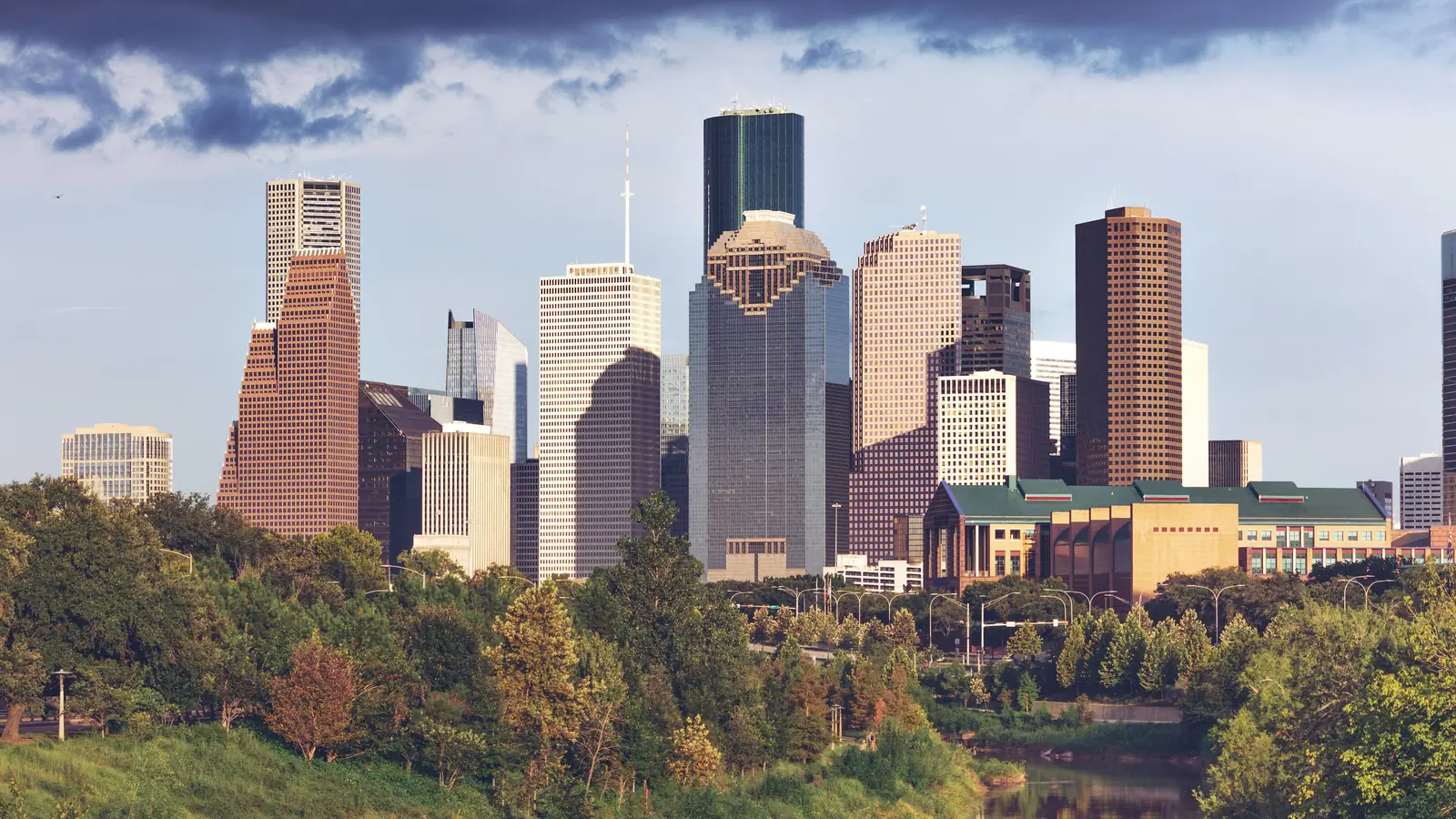 Downtown Houston's skyscrapers in warm evening light above the trees along Buffalo Bayou.