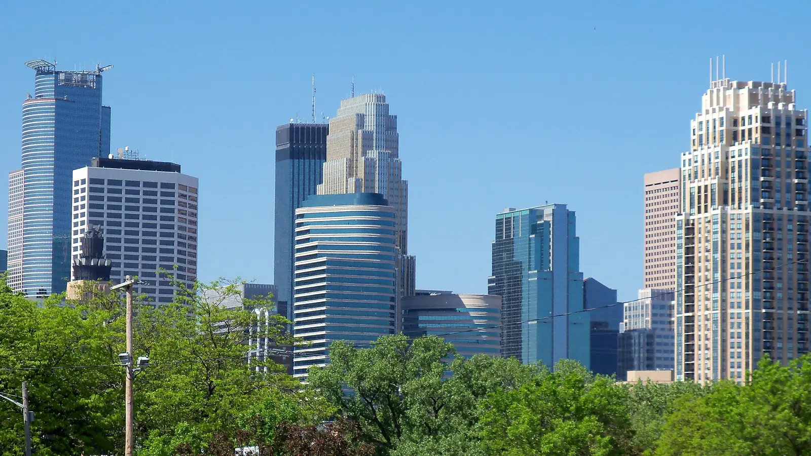 The Minneapolis skyline above green trees on a clear day.