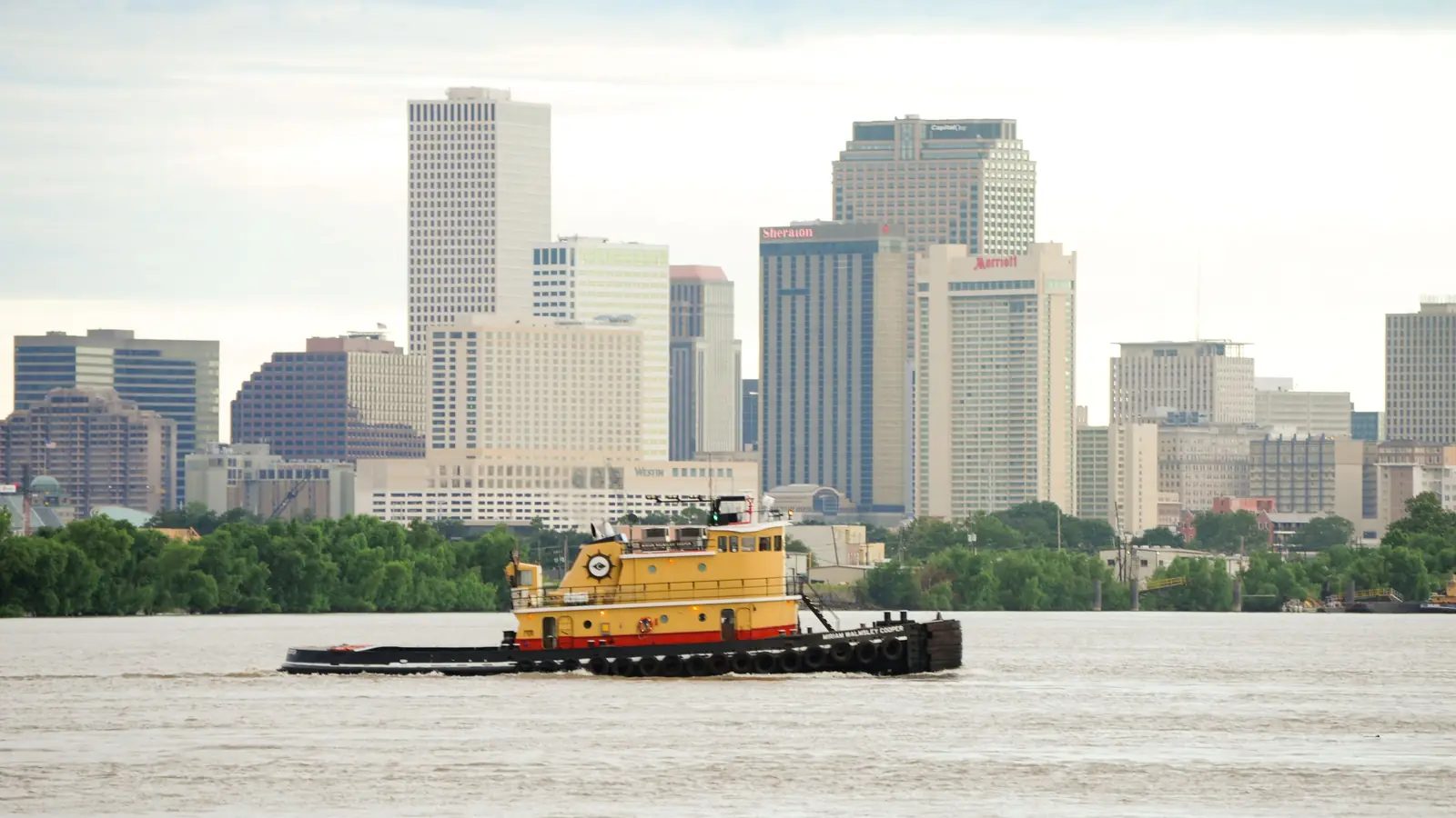 The New Orleans skyline across the Mississippi River with a tugboat in the foreground.
