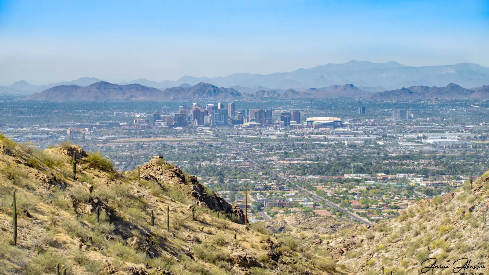 Downtown Phoenix and the wide Valley of the Sun seen from a desert ridge, mountains on the horizon.