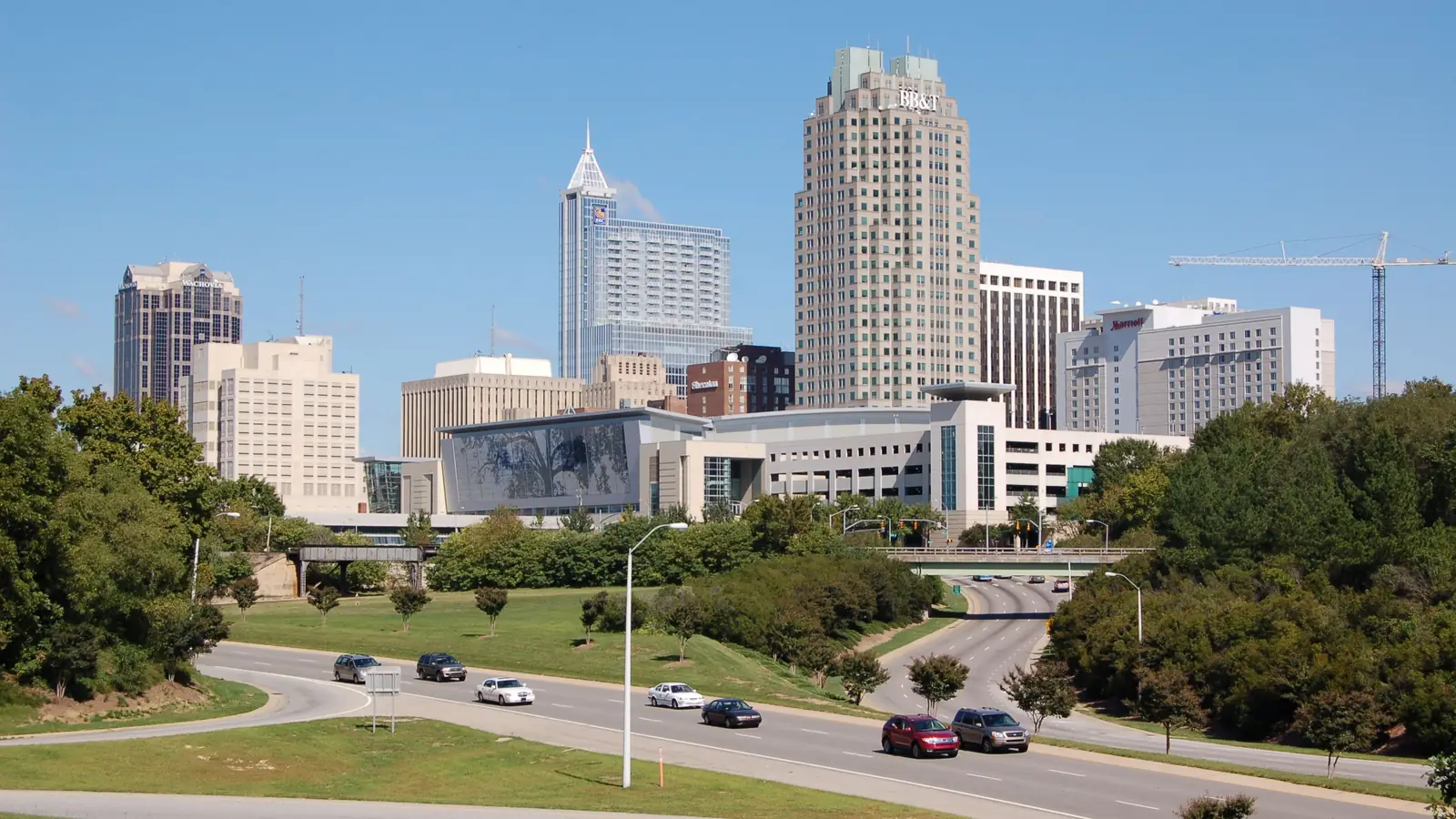 The downtown Raleigh skyline above the trees and Western Boulevard on a clear day.