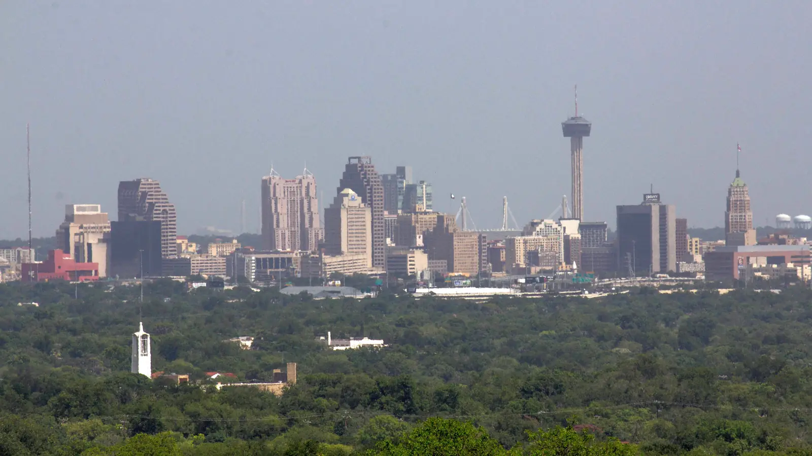 The San Antonio skyline and the Tower of the Americas rising above a green tree canopy.