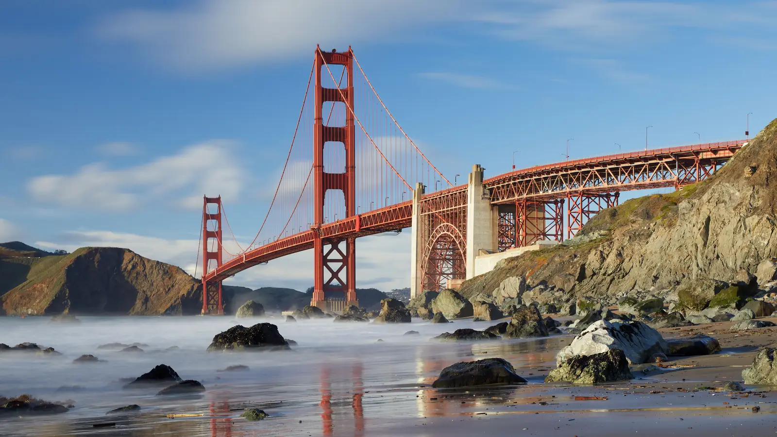 The Golden Gate Bridge in San Francisco from Marshall’s Beach in the Presidio, with smooth water around the rocks in late-day light.