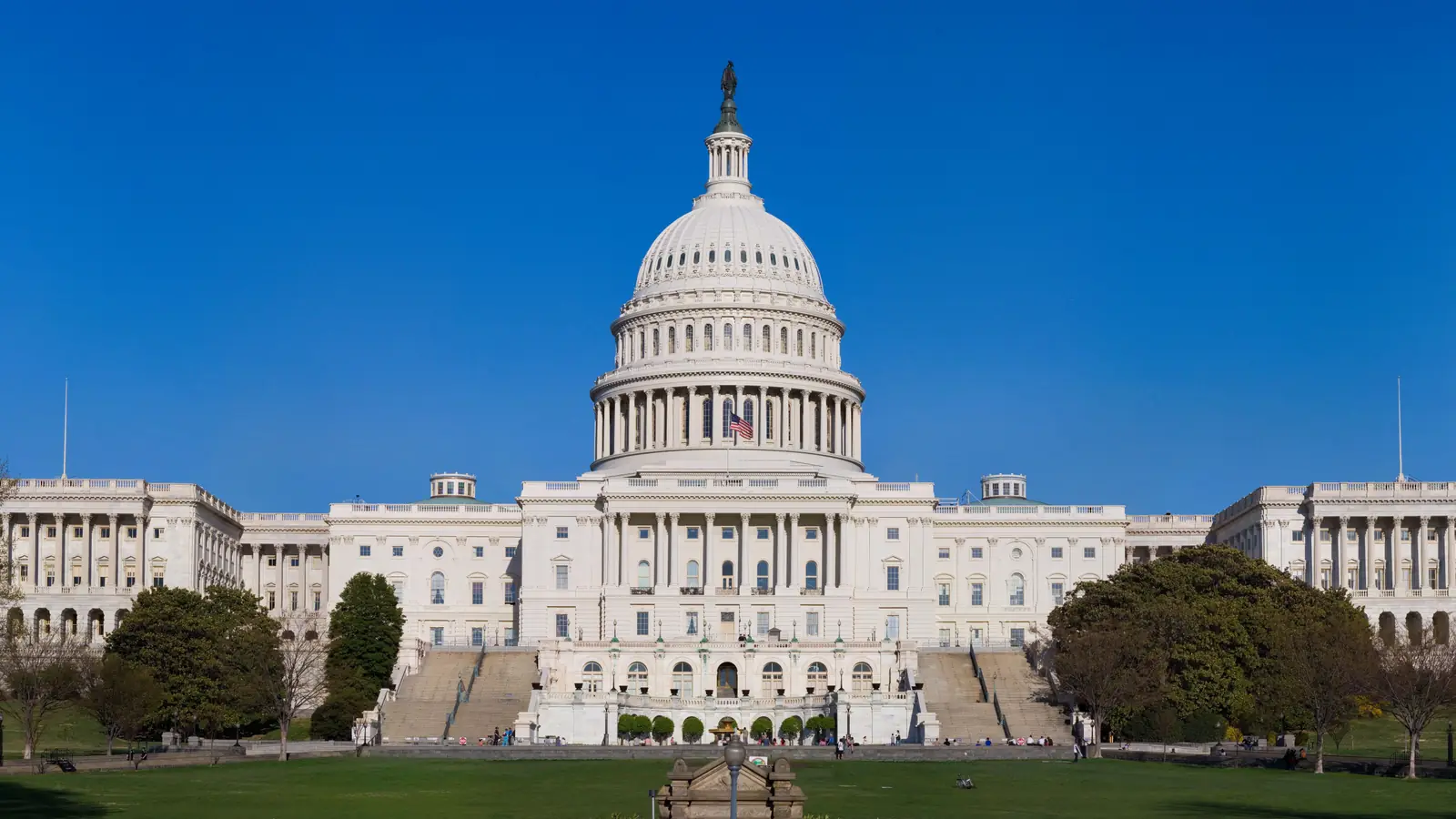 The west front of the United States Capitol in Washington, DC, under a clear blue sky.